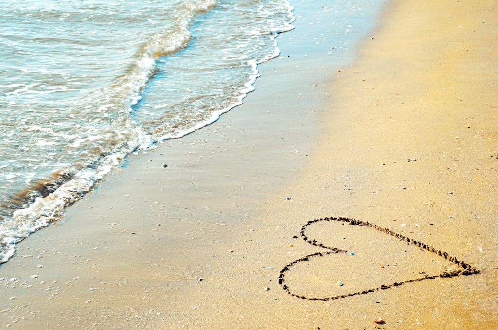 A heart drawn in the sand with waves approaching on a sunny beach day.